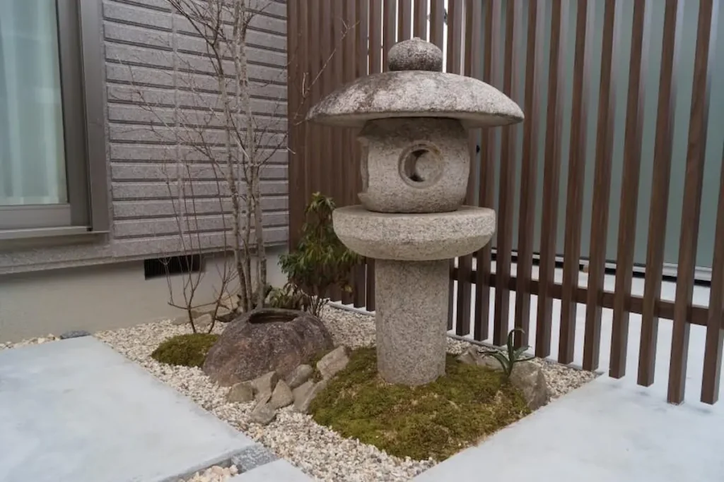 A traditional Japanese stone lantern and a rustic rock water basin placed in a minimalist moss and gravel garden corner.
