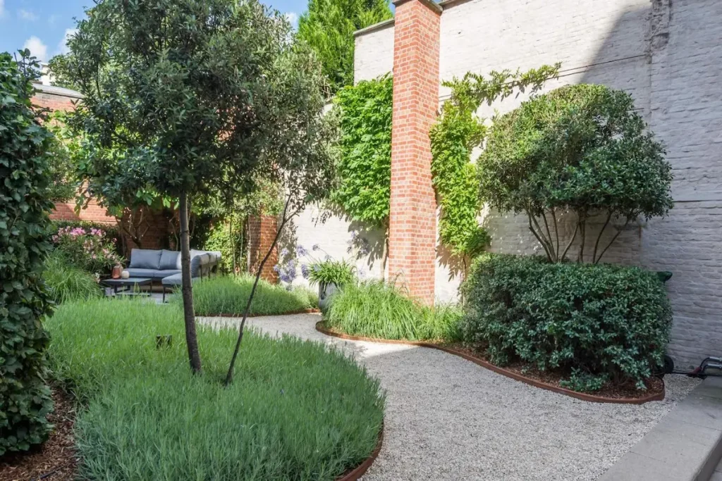 Low-maintenance backyard landscape design with resilient perennial plants, gravel path, and modern structural greenery.