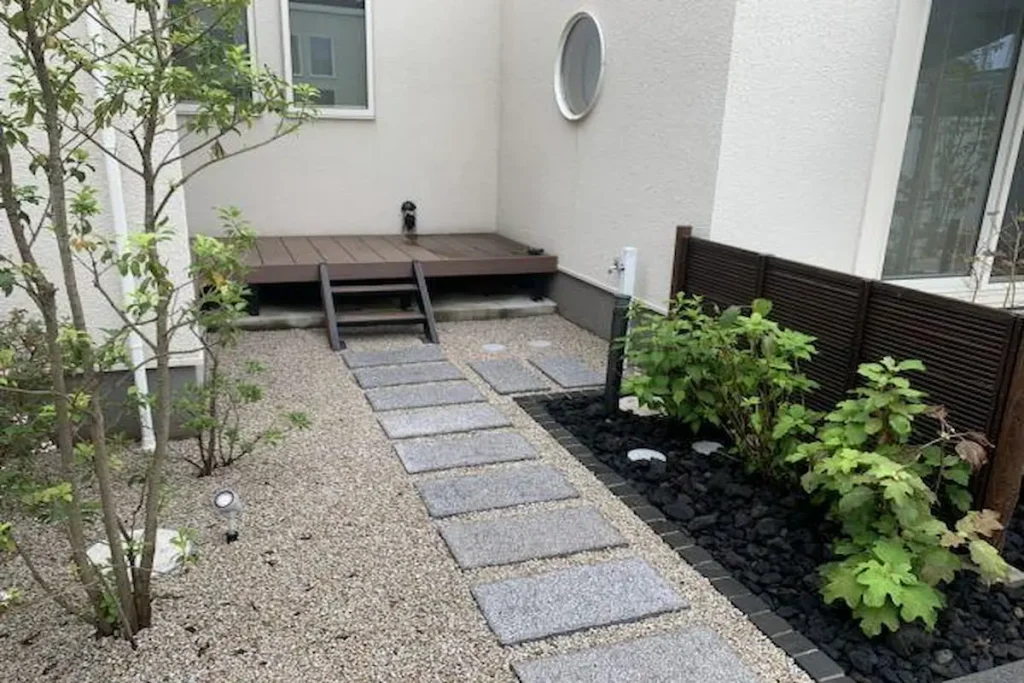 A Japanese Zen courtyard garden with a grey granite stepping stone pathway, fine gravel groundcover, and a wooden patio deck.