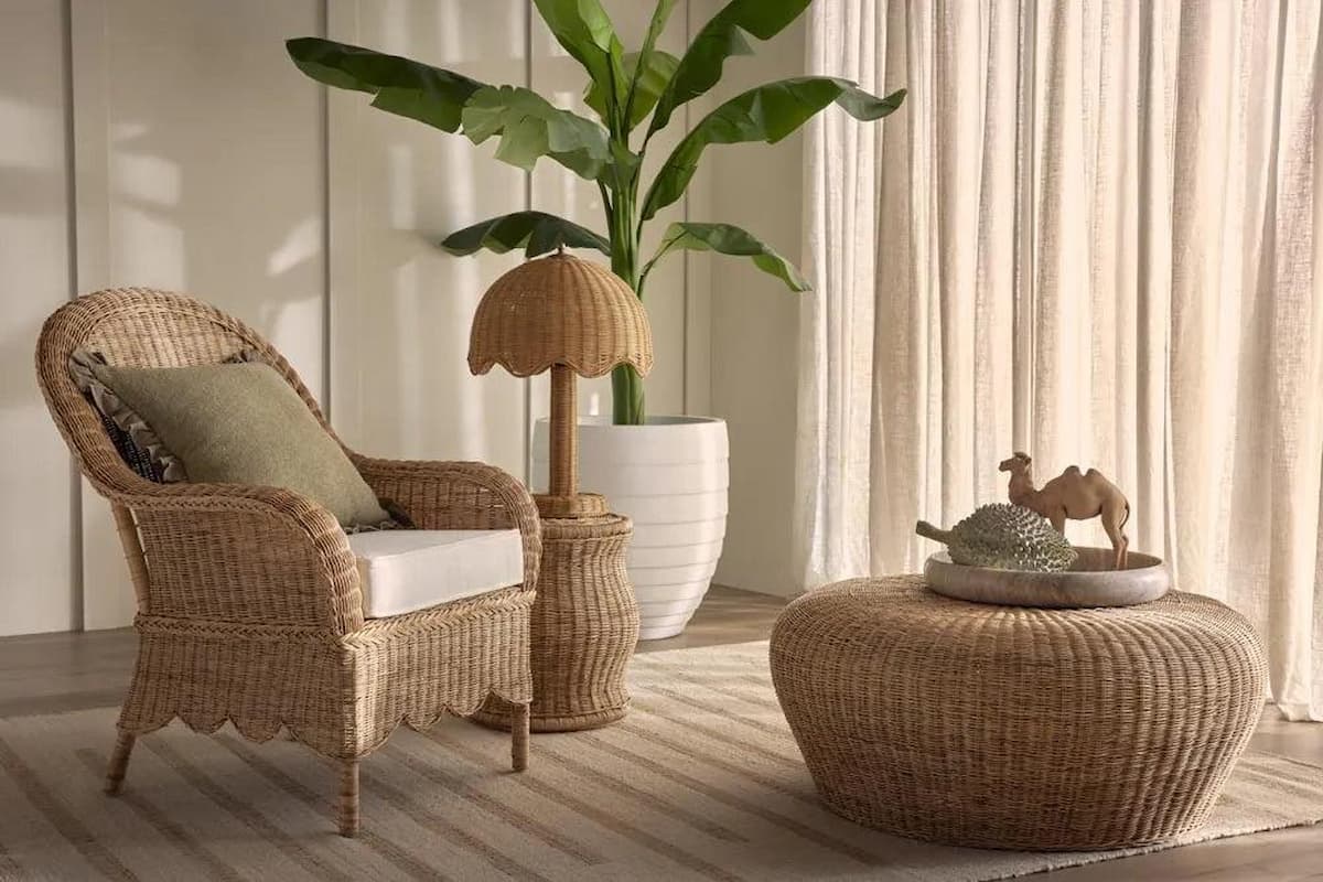 Hamptons style reading nook with a scalloped wicker armchair, rattan ottoman, and neutral linen curtains.