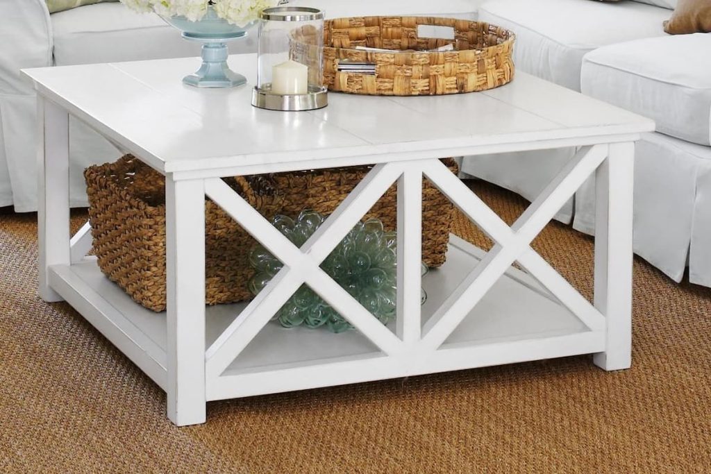 White painted rubberwood coffee table with X-brace design and bottom storage shelf in a coastal living room.