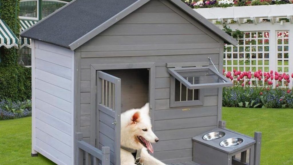 Traditional A-frame timber dog house with a weatherproof shingle roof, elevated legs, and front entrance in a grassy backyard.