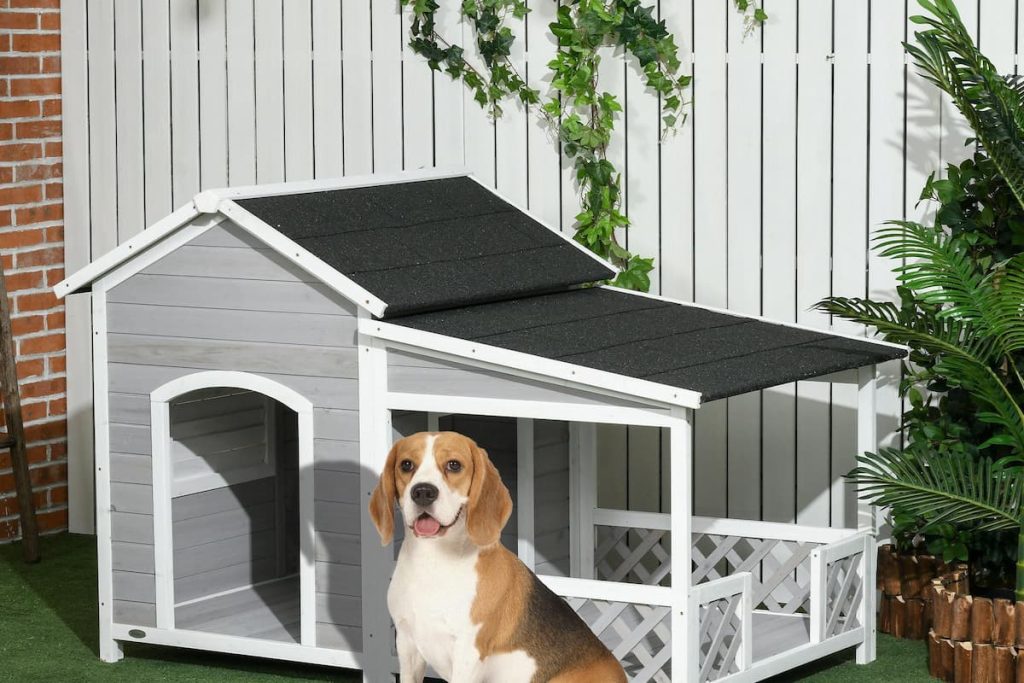 Classic A-frame timber dog house with a grey asphalt shingle roof and elevated floor base on a rustic stone patio.