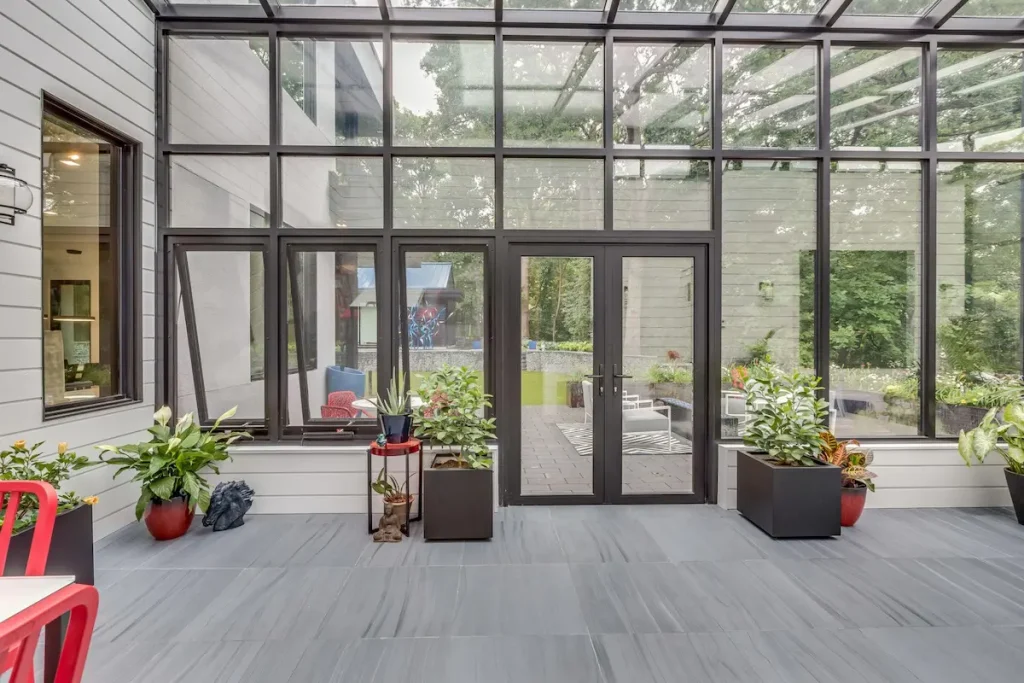 A minimalist sunroom interior with dark-framed glass wall grilles and potted plants on gray slate flooring.