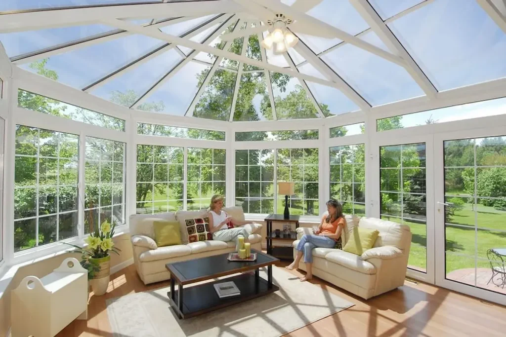 A traditional white-framed Victorian sunroom conservatory exposed to direct bright sunlight over a living furniture setup.